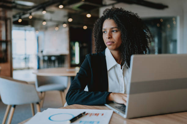 istock Young businesswoman using laptop at table looking to side 1908372056