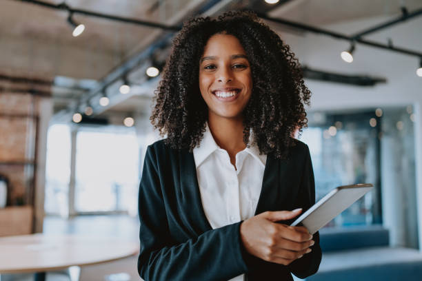 retrato de una mujer de negocios mirando a la cámara sonriendo sosteniendo la tableta digital - frizzy 20s adult african descent fotografías e imágenes de stock