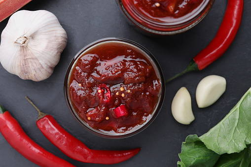 Tasty rhubarb sauce and ingredients on black table, flat lay