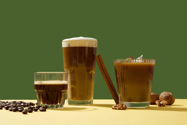 コーヒー豆、シナモンスティック、クルミで緑の背景に飾られたクリーミーな泡とコーヒーのさまざまなおいしいカップ。朝に一杯のコーヒーを飲むと、より注意力が強くなり、活動的にな� - coffee crop cup coffee bean coffee ストックフォトと画像