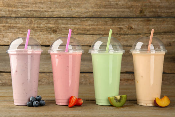 istock Plastic cups with different tasty smoothies and fresh fruits on wooden table 1908421783