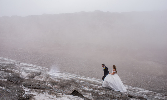 portrait of a couple wearing their wedding dresses while walking through the middle of the snowy field on stone