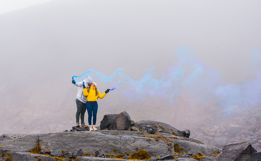 portrait of a beautiful couple embracing on a snowy mountain and in the middle of volcanic stones and releasing blue smoke
