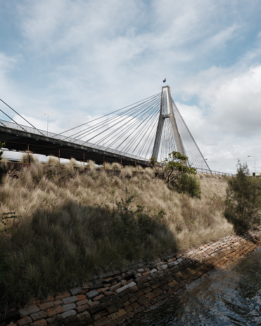 View of a suspension bridge over a grassy hill with cloudy blue sky.