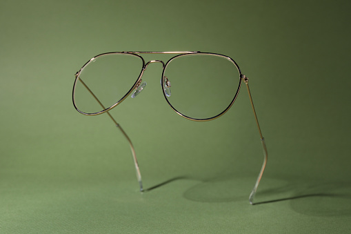 Stylish pair of glasses with metal frame on olive background