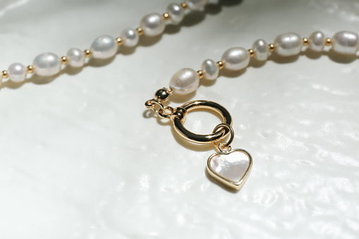 Elegant pearl necklace on white textured background, closeup