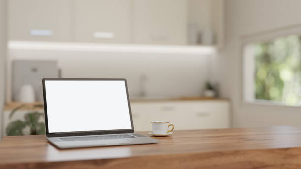 istock A white-screen laptop mockup and a coffee cup on a wooden table in a minimalist white kitchen. 1908481717