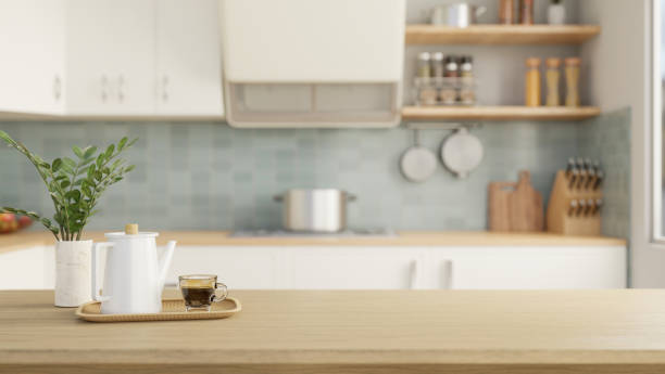 Close-up image of a wooden tabletop with a coffee pot, a coffee cup, and a copy space for display your product over a blurred background of a modern kitchen. 3d render, 3d illustration