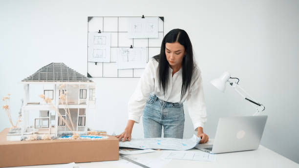 istock Architect puts blueprint on the table and compares with house model. Immaculate. 1908500803