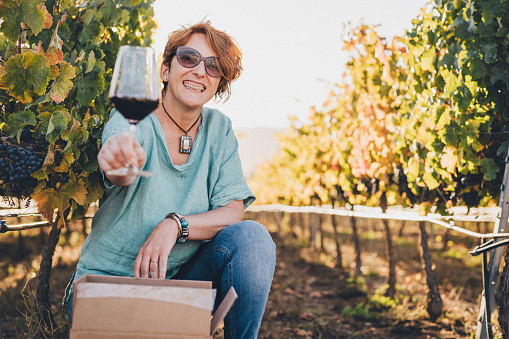 Winemaker woman offering a glass of wine in the vineyard