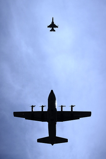 The photo forms a silhouette of a military transport plane flying after a fighter plane.