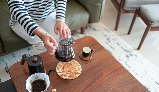 Woman enjoying a coffee ritual at home. She shaking to mix coffee prepared in an alternative way using a dripper and a paper filter