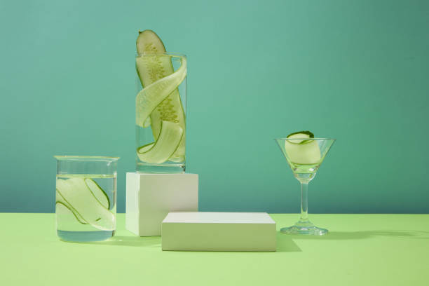istock Thinly sliced cucumber slices inside a glass are placed next to two white platforms on a blue background. Empty space for product display. Copy space. 1908572547