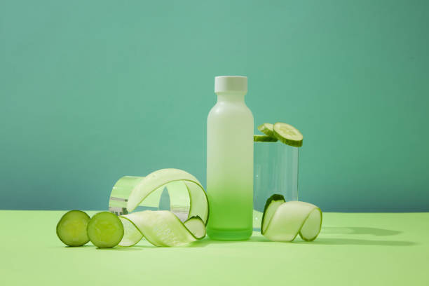 istock Front view of an empty bottle, a glass and thinly sliced cucumbers on display. Copy space for ads. Healthy fresh fruit concept. Body care with natural product. 1908574113
