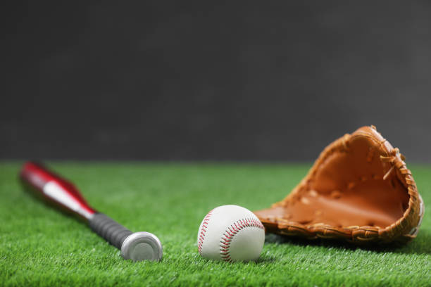 istock Baseball bat, leather glove and ball on green grass against dark background. Space for text 1908631367