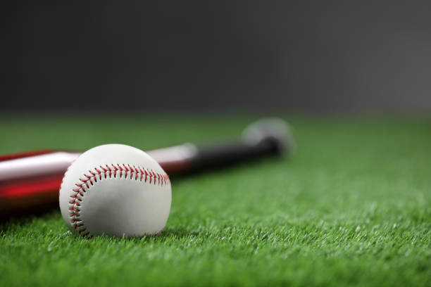 istock Baseball bat and ball on green grass against dark background, closeup. Space for text 1908631876