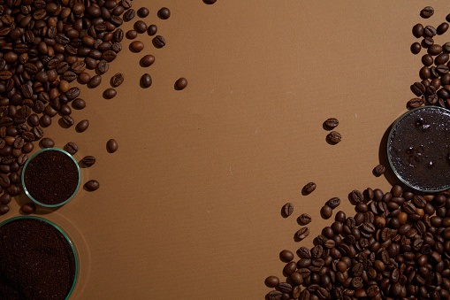 Many coffee beans decorated on brown background with petri dishes of coffee grounds. Space for design. Coffee is rich in linoleic acid which helps increase skin elasticity and anti-inflammation.