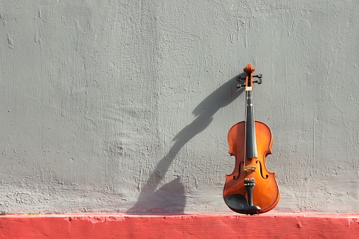 A photo of a violin is placed on the side of an old wall. Suitable as a background image for various design needs, quotes, posters, etc.