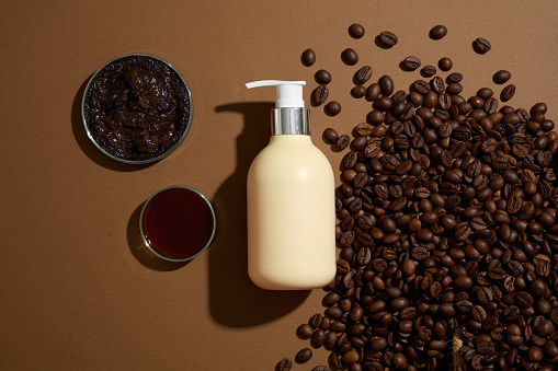 Scene for advertising product with natural ingredient and mockup for design. Top view of a pump bottle container for shampoo or lotion decorated with coffee beans on brown background