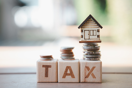 House model and growth of stack of coins on wooden blocks word TAX. Prepare budget for reduce Property Tax. Mortgage, loan, repayments, credit limit, business and financial concept.