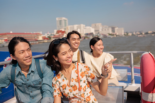 Group of smiling friends enjoys sightseeing the city from the boat.