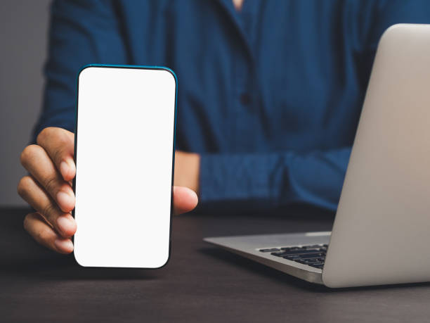 istock Businesswoman holding a white blank screen smartphone vertically while sitting at the table 1908687606