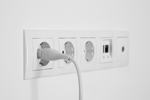 Many power sockets with plug, ethernet and TV coax plates on white wall indoors