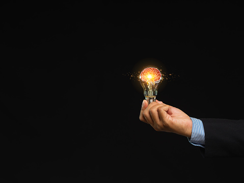 Close-up of hand a businessman holding a lighting bulb with lighting while standing on a black background. Illuminating success and creative thinking. Vision and Strategy for Entrepreneurs.
