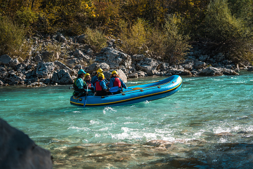 An energetic Caucasian mother and her three mixed-race kids team up with a guide for an exhilarating rafting journey, equipped with helmets and paddles.