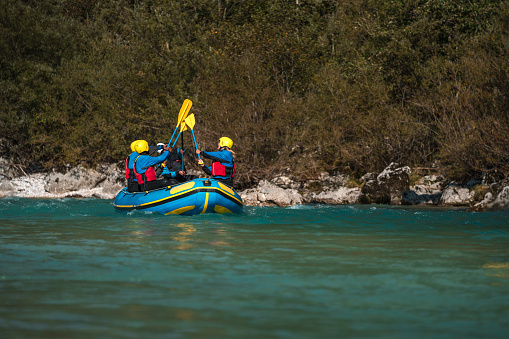 A group of diverse rafters, geared in protective helmets and life vests, paddle in unison through a river, showcasing teamwork and determination.