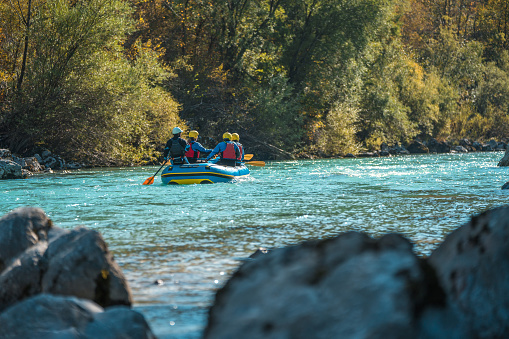 A group of mature rafters wearing safety gear paddle a raft amidst the changing leaves of a serene river landscape.