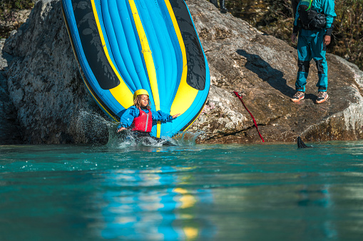 The river rock becomes a hub of joy as rafting enthusiasts, young and old, embrace an improvised raft slide, their cheer echoing off the water.