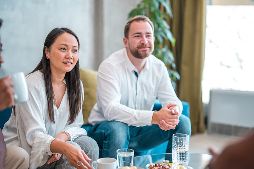 Trendsetting colleagues, representing diverse backgrounds, participate in a coffee break in a modern office space, seated comfortably, and fostering a relaxed atmosphere.