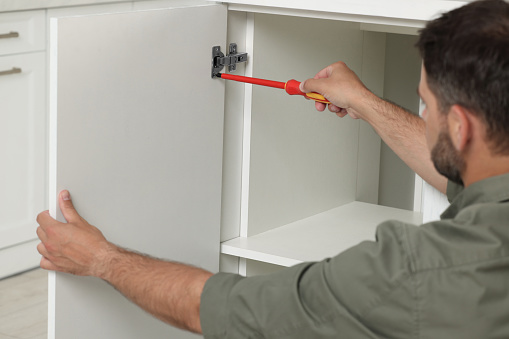 Man with electric screwdriver assembling furniture indoors, closeup