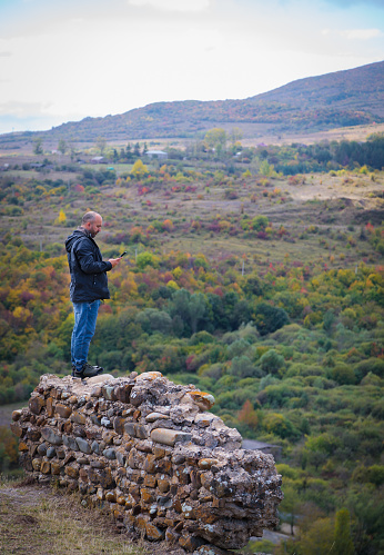 A man standing on a ruined fortress wall, admiring the scenic mountain view on a beautiful sunny day. The ancient stone structures provide a striking contrast against the majestic natural landscape.
