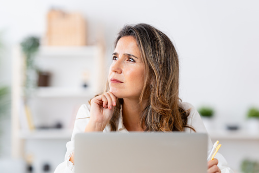 Pensive woman looking away while working from home using laptop