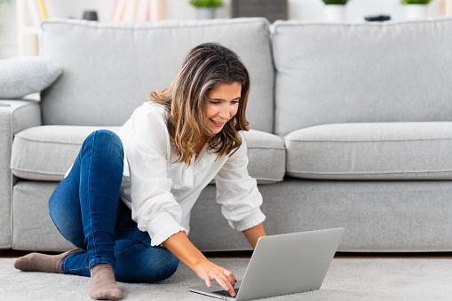 Woman using laptop sitting on the floor of the living room