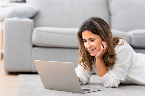 Relaxed woman using laptop lying down in the floor at home