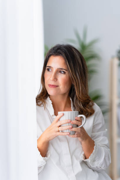 istock Woman leaning on the window and drinking coffee at home 1908856327
