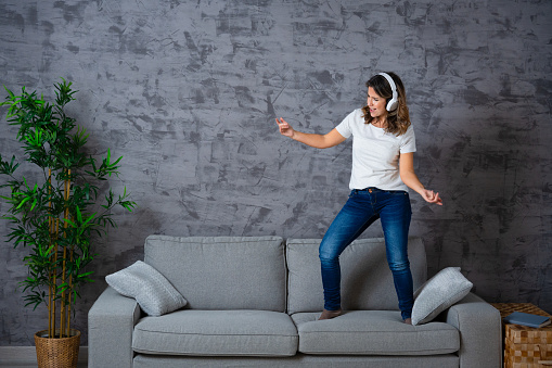 Woman dancing on the sofa listening to music with headphones