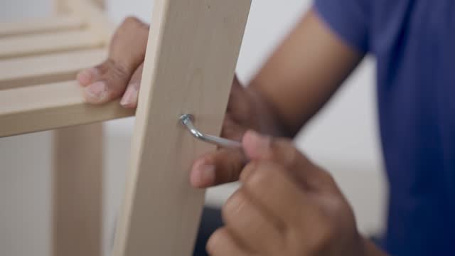 Close-up of the hand of a man going to tighten a nut with a tool. There is a wooden piece of furniture in the picture.