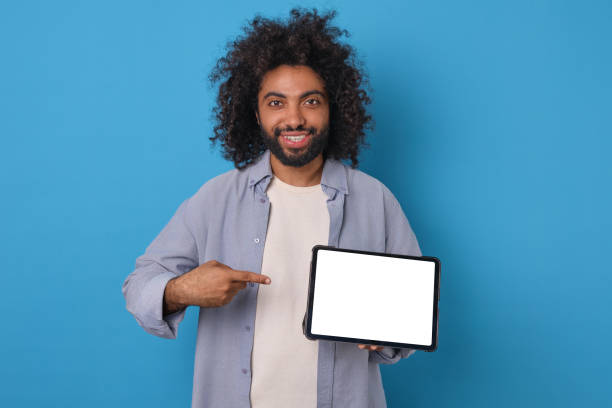 istock Young Arabian man holding tablet computer with white screen stands in studio 1908870893