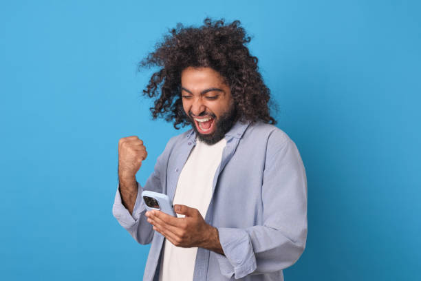 istock Young Arabian man happy waves hand after receiving SMS in phone stands in studio 1908871468