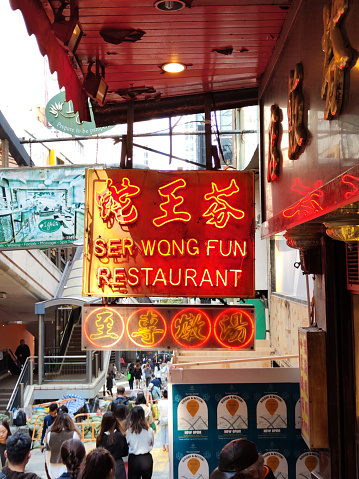 Iconci Ser Wong Fun restaurant neon placard in Central Hong Kong Island. People walking on the street.