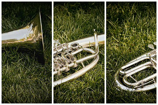 Closeup of a musical wind instrument orchestra of silver trumpets on a green grass in a city park.