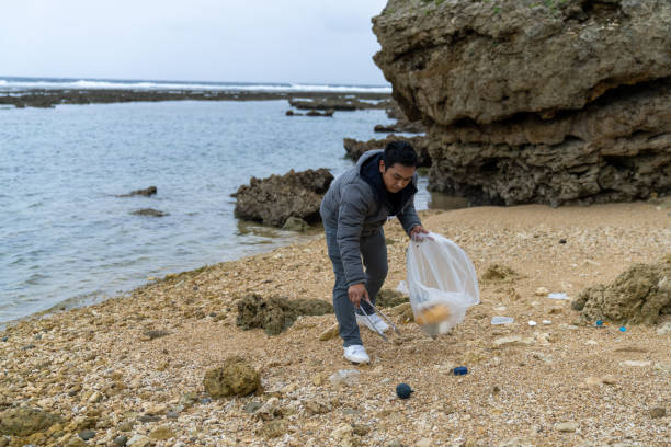 istock Mid adult male cleaning up various plastic waste on a beach 1909002514