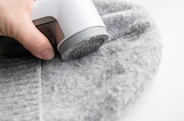 istock Person hand using sheaving lint balls from winter hat with lint shaver machine tool. Clothes maintenance concept. 1909018893