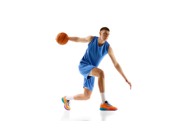 istock Dynamic image of young man in blue uniform, basketball player in motion during game, dribbling ball isolated over white background. Sport concept 1909076739