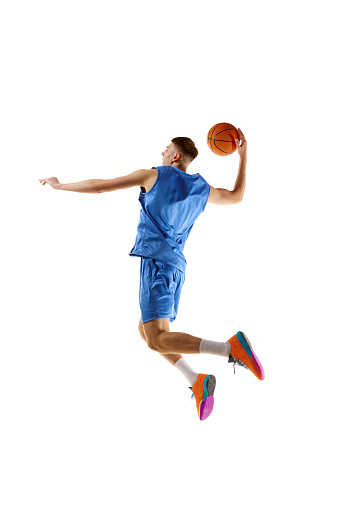 Slum dunk. Full-length image of young guy, basketball player in motion, jumping with ball isolated over white background. Concept of sport, competition, match, championship, health, action. Ad