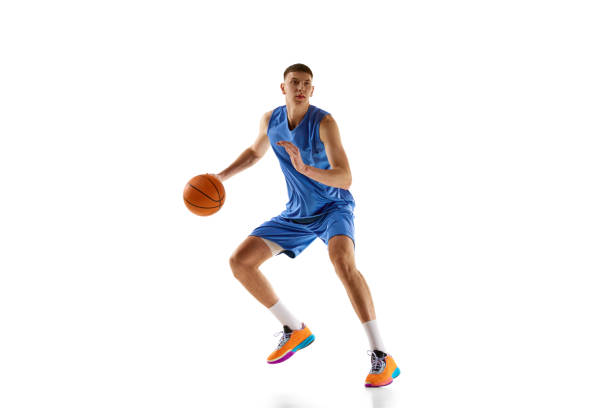 istock Dynamic image of young man in blue uniform, basketball player in motion during game, dribbling ball isolated over white background. Sport concept 1909077257